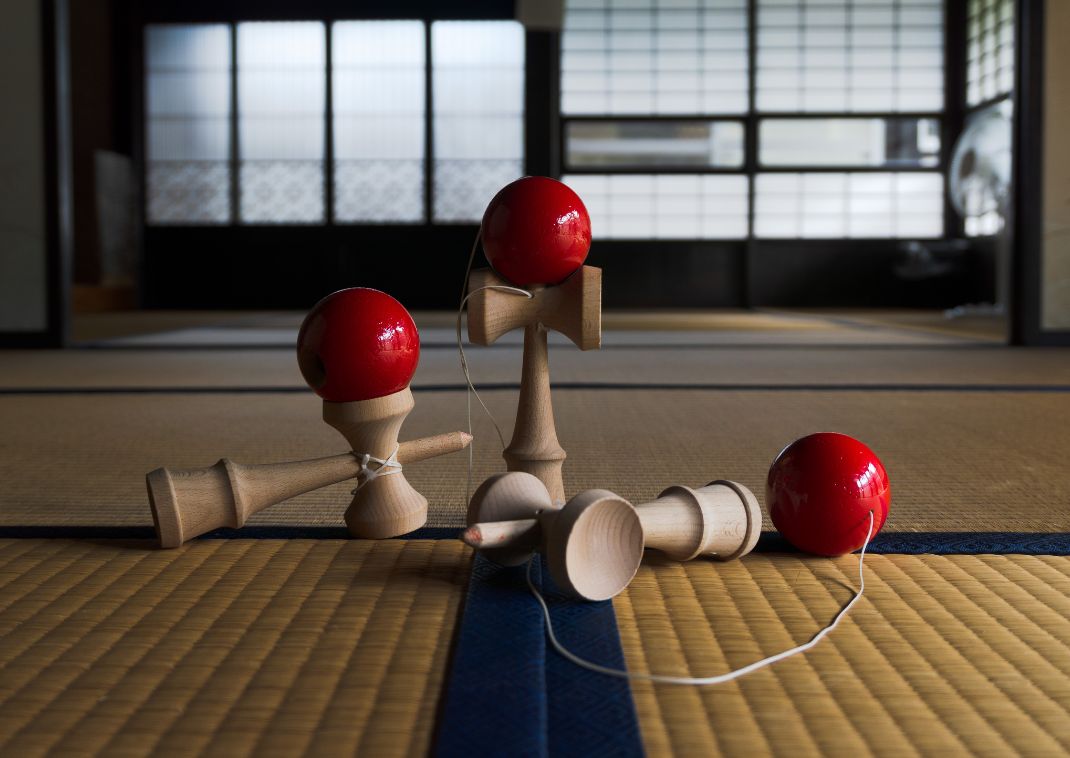 Tres juguetes de madera kendama con bolas rojas descansan sobre un suelo de tatami en una habitación japonesa tradicional.