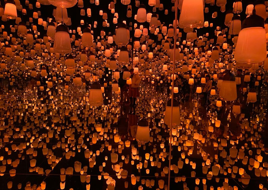 Instalación artística con cientos de lámparas colgantes reflejadas en espejos, creando un efecto infinito de luces cálidas.