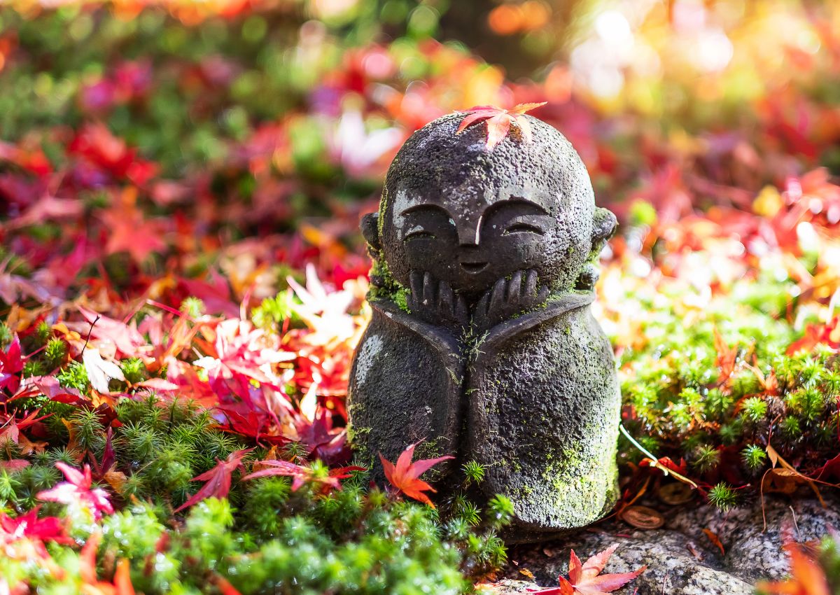 Estatua Jizo con una hoja de arce rojo cayendo en el jardín japonés del templo Enkoji, Kioto, Japón.