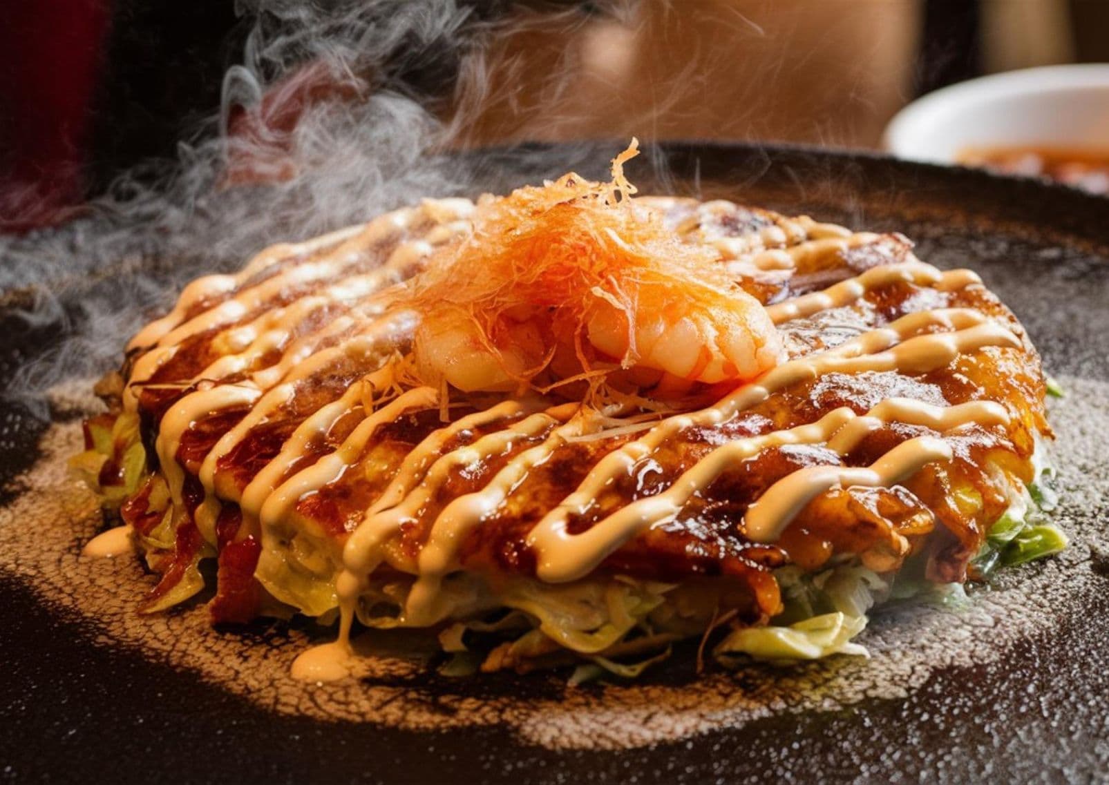 Okonomiyaki japonés siendo preparado en el momento en una plancha de hierro caliente