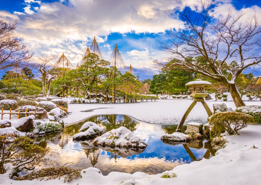 Jardín japonés cubierto de nieve con estanque y linterna de piedra.