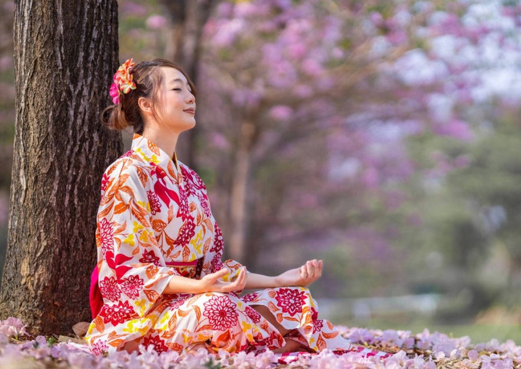 Mujer japonesa meditando durante la temporada de flor de cerezo para paz interior y atención plena.
