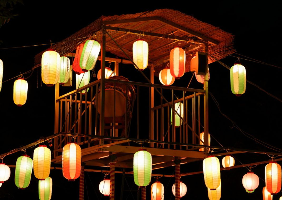 Torre de madera elevada (yagura) decorada con farolillos de papel de colores iluminados por la noche durante el festival japonés Bon Odori.