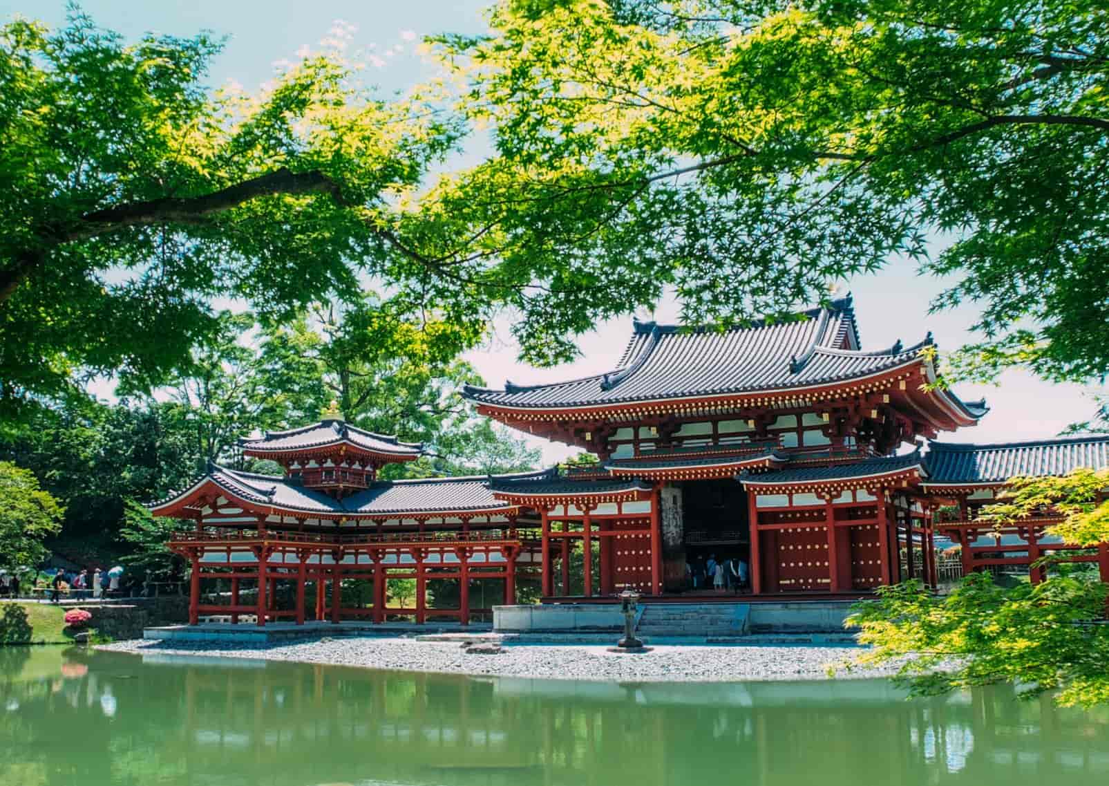 El templo Byodo-in, de color rojo brillante, en Uji, Kioto, reflejado en el agua junto a las hojas verdes de los arces
