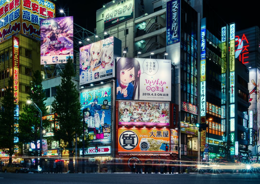 Carteles y anuncios de anime iluminados y coloridos cubriendo edificios en un distrito urbano concurrido por la noche