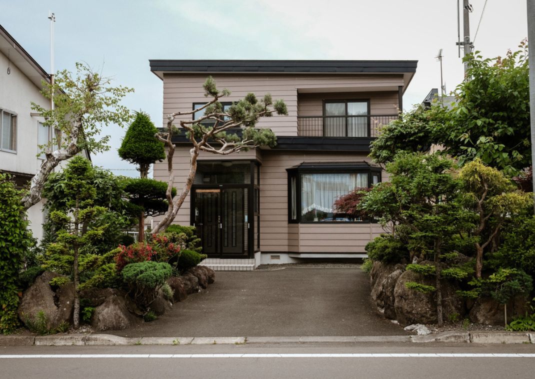 Casa japonesa moderna con un jardín bien cuidado y árboles decorativos en el patio delantero.