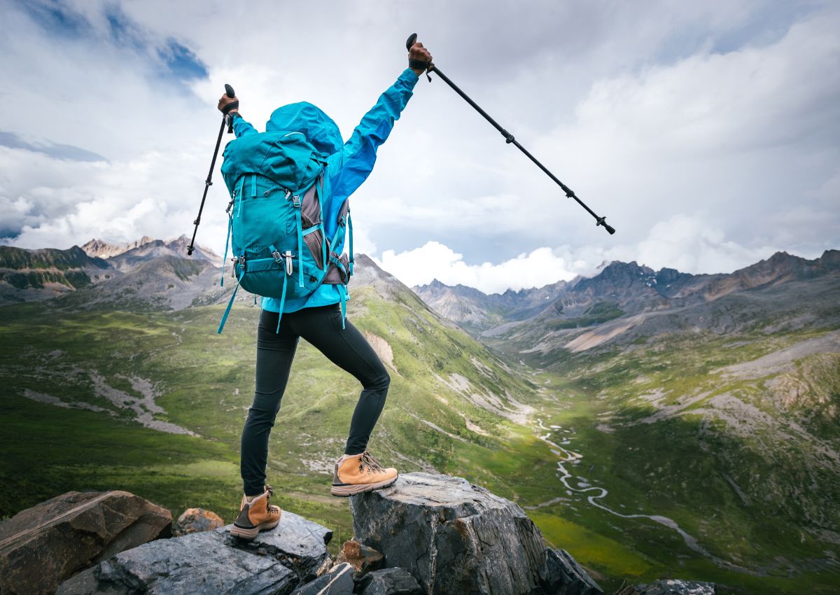 Excursionista con mochila y bastones de senderismo en la cima de una montaña de gran altitud