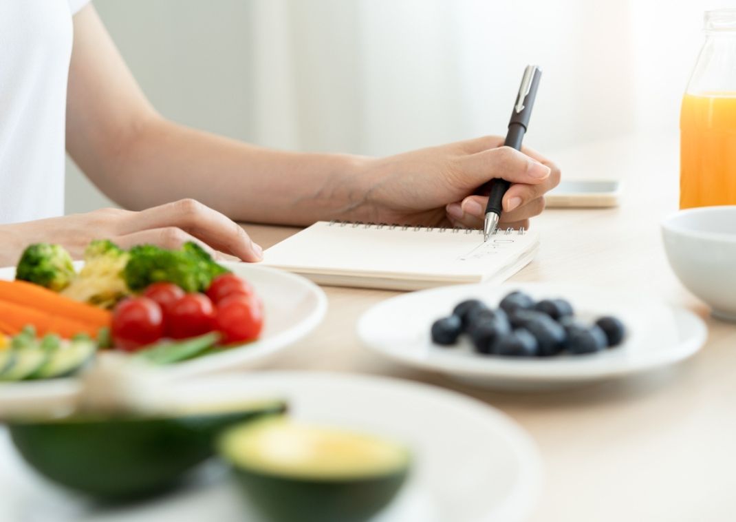 Mujer escribiendo rodeada de fruta saludable