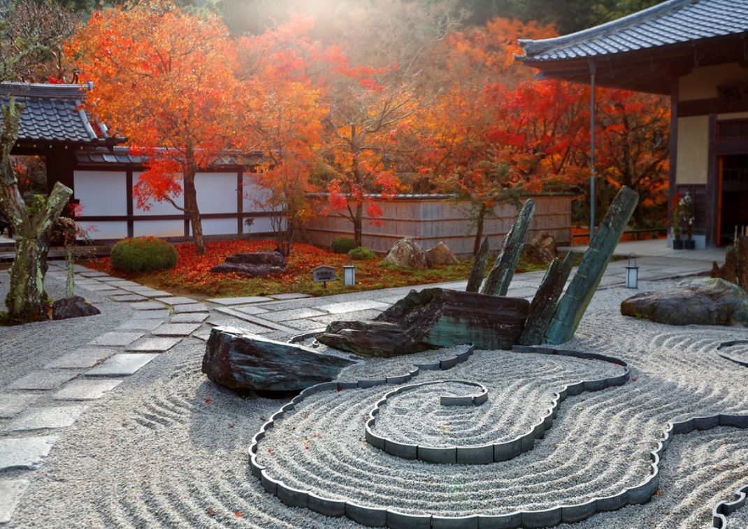 Jardín zen japonés con árboles de hojas rojas y rocas decorativas.