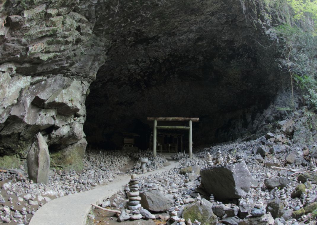 Entrada a un santuario en una cueva con un torii y cientos de ofrendas de piedras apiladas en Yamato, Japón