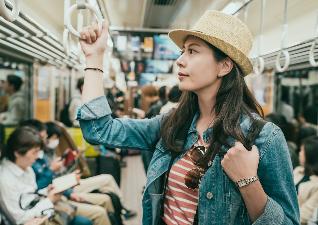 Joven viajero asiático de pie en el metro de Japón, sujetándose al asidero con una mano