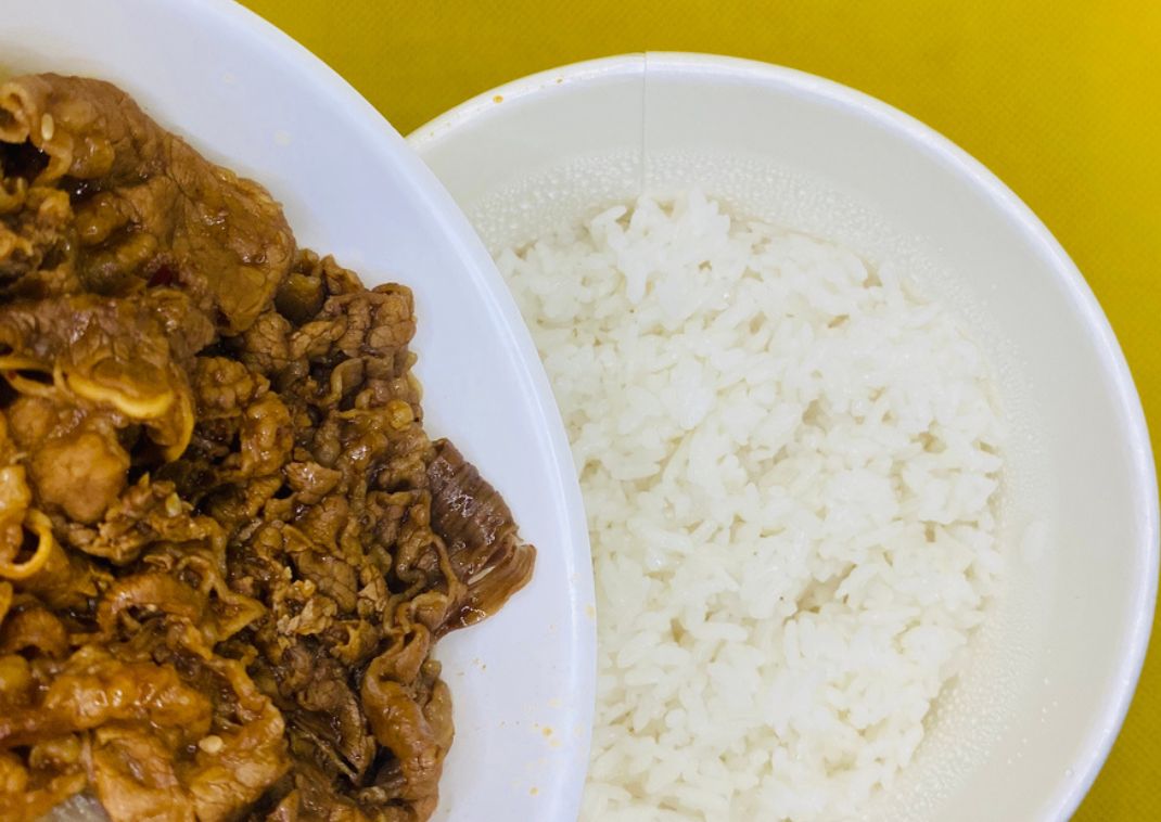 Cuenco japonés de ternera (gyudon) servido con un bol separado de arroz blanco sobre fondo amarillo.
