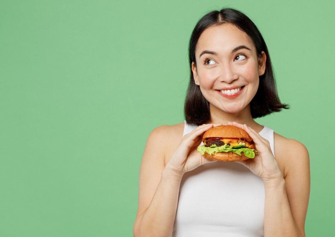 Mujer sosteniendo una hamburguesa sobre un fondo verde