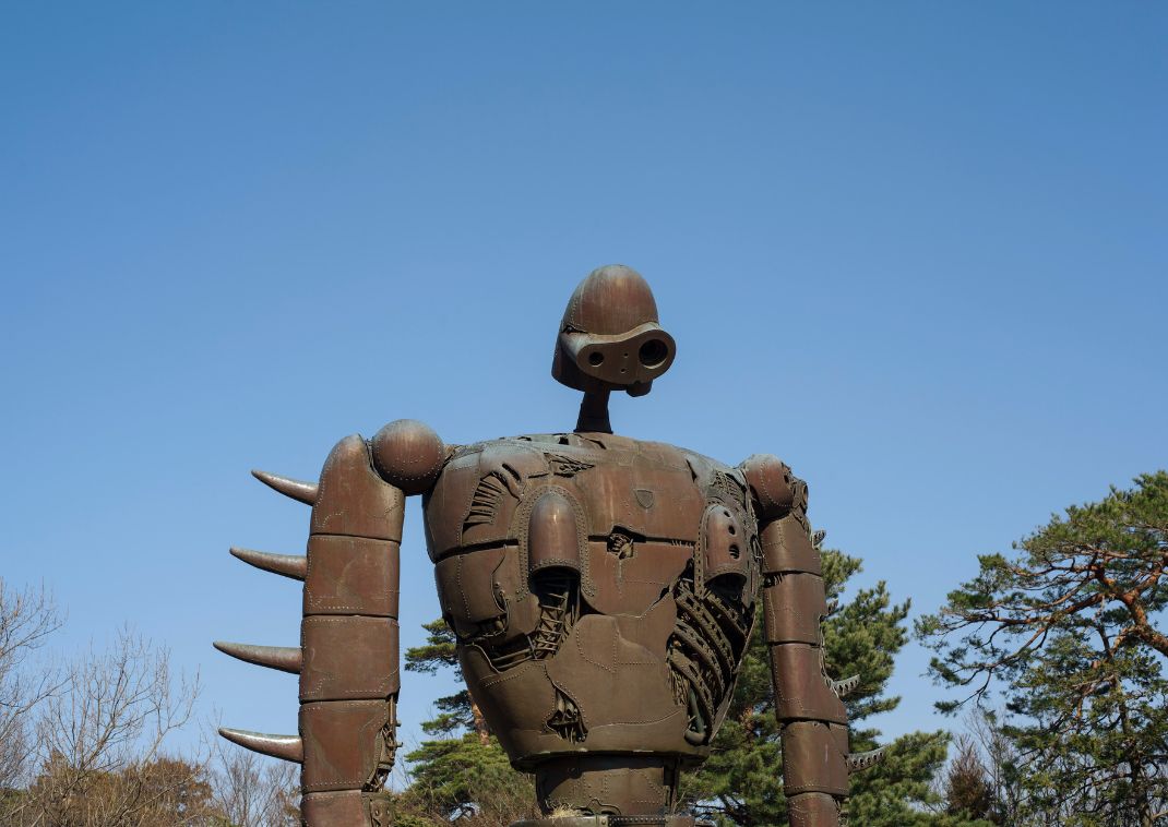 Gran estatua de robot color óxido con detalles mecánicos al aire libre bajo un cielo azul despejado y árboles