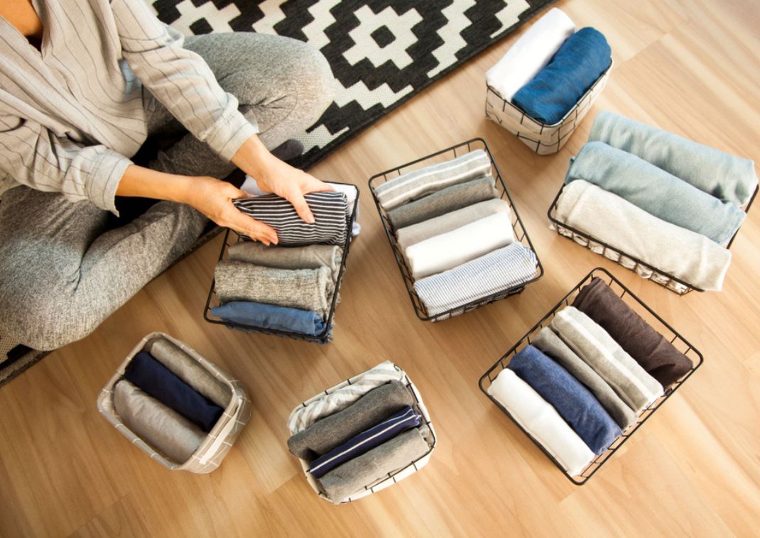 Persona sentada en el suelo organizando y doblando ropa en cestas usando el método KonMari.