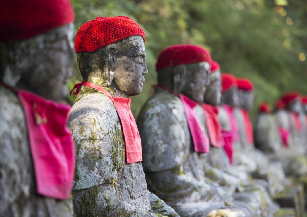 Fila de estatuas de piedra con gorros y baberos rojos en un entorno natural.