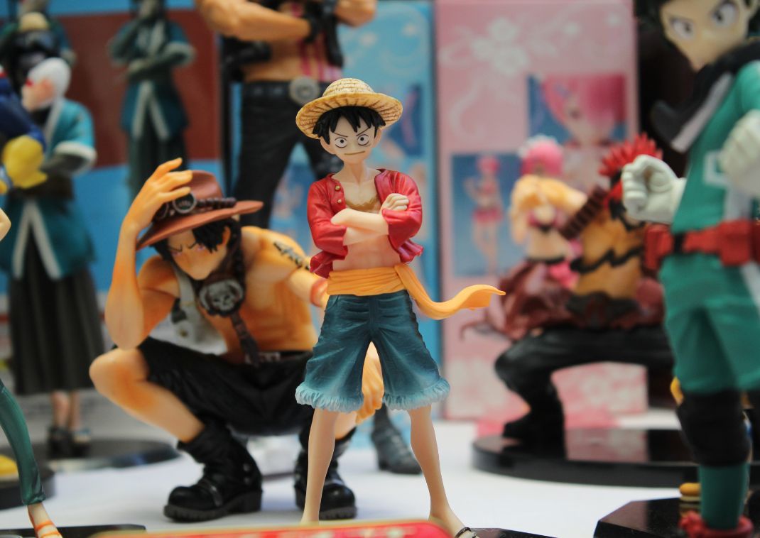 Colección de figuras de personajes de anime en exhibición, con una figura de sombrero de paja y chaqueta roja en primer plano