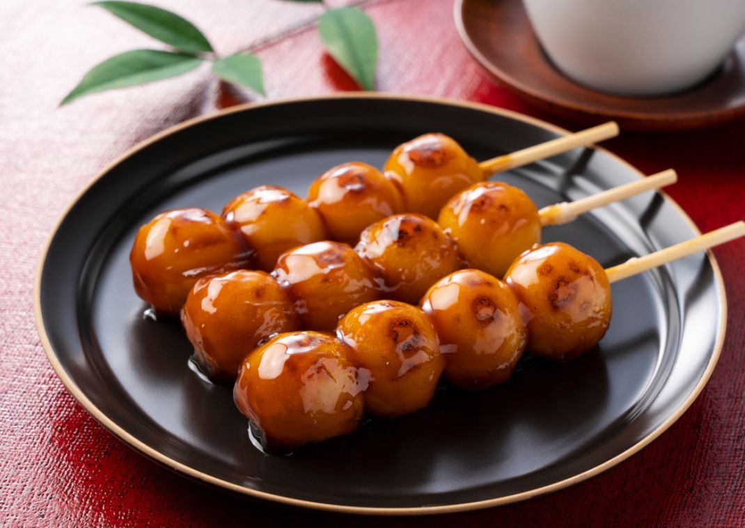 Brochetas de bolitas de arroz dango japonesas a la parrilla cubiertas con glaseado de soja dulce en un plato negro.
