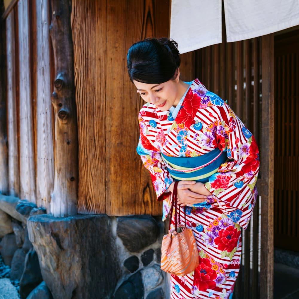 Mujer japonesa con un colorido kimono haciendo una reverencia delante de un edificio tradicional de madera en Kioto.