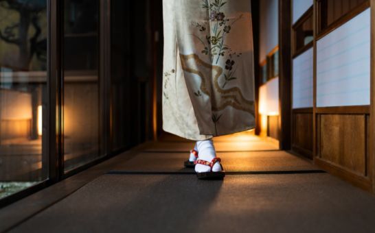 Mujer con kimono paseando por un ryokan tradicional con esteras tatami y puertas shoji.