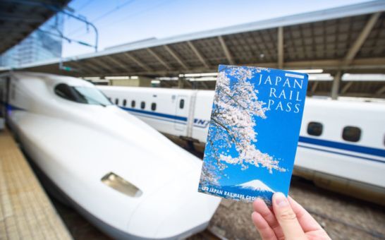 Mano que sostiene un billete del Japan Rail Pass delante de un Shinkansen en la estación de Tokio