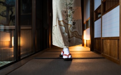 Mujer con kimono paseando por un ryokan tradicional con esteras tatami y puertas shoji.