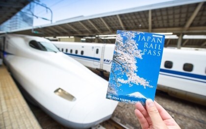 Mano que sostiene un billete del Japan Rail Pass delante de un Shinkansen en la estación de Tokio