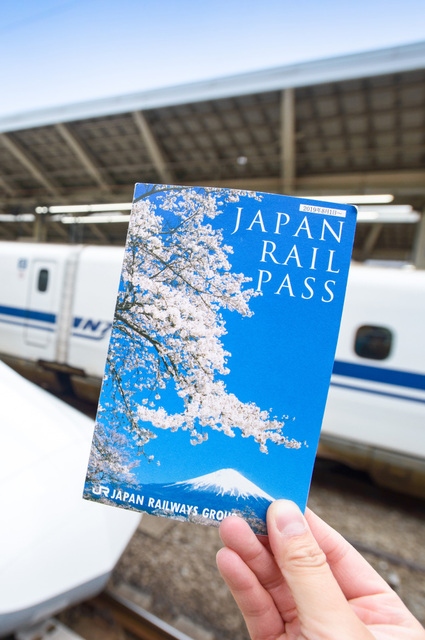 Mano que sostiene un billete del Japan Rail Pass delante de un Shinkansen en la estación de Tokio
