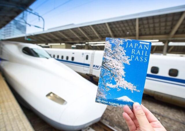 Mano que sostiene un Japan Rail Pass delante de un tren shinkansen en Japón