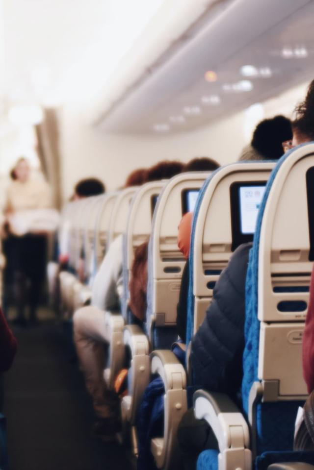 Interior de un gran avión de pasajeros con gente sentada y una azafata de uniforme caminando por el pasillo.